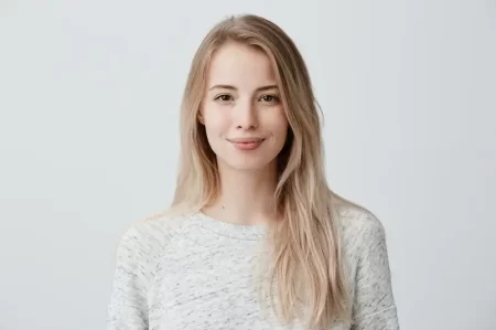 Pretty smiling joyfully female with fair hair, dressed casually, looking with satisfaction at camera, being happy. Studio shot of good-looking beautiful woman isolated against blank studio wall.